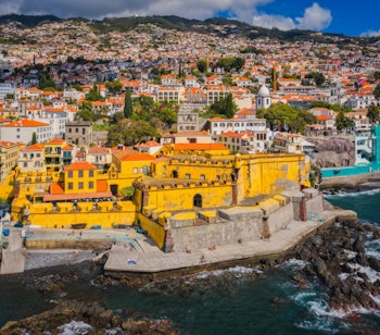 Luftfoto af den historiske gule fæstning Forte de São Tiago fra 1600-tallet ved kysten i Funchal på Madeira, hvor Restaurante do Forte serverer middag med udsigt over Atlanterhavet