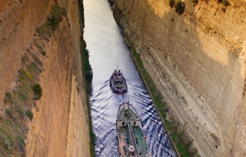 Fragtskib sejler gennem den smalle Korinthkanal i Grækenland med høje klippevægge på begge sider af den historiske vandvej