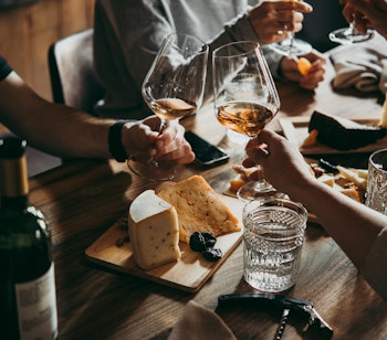 Venner der nyder en autentisk fransk oplevelse med vinsmagning og oste serveret på træbræt i hyggelig restaurant-atmosfære, der viser den sociale madkultur