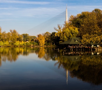Fredfyldt sø i Beograd med gyldne efterårstræer og tårnrefleksion i det stille vand, perfekt til naturoplevelser i Serbien