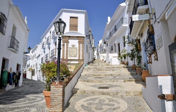 Charmerende hvid bjerglandsby i Frigiliana, Andalusien med traditionelle hvidkalkede huse, smalle brostensbelagte gader og blomsterkrukker i solskinsvejr