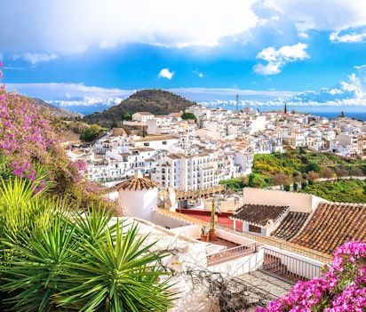 Idyllisk gadeparti i den hvide landsby Frigiliana i Andalusien med traditionel spansk arkitektur og farverige blomster