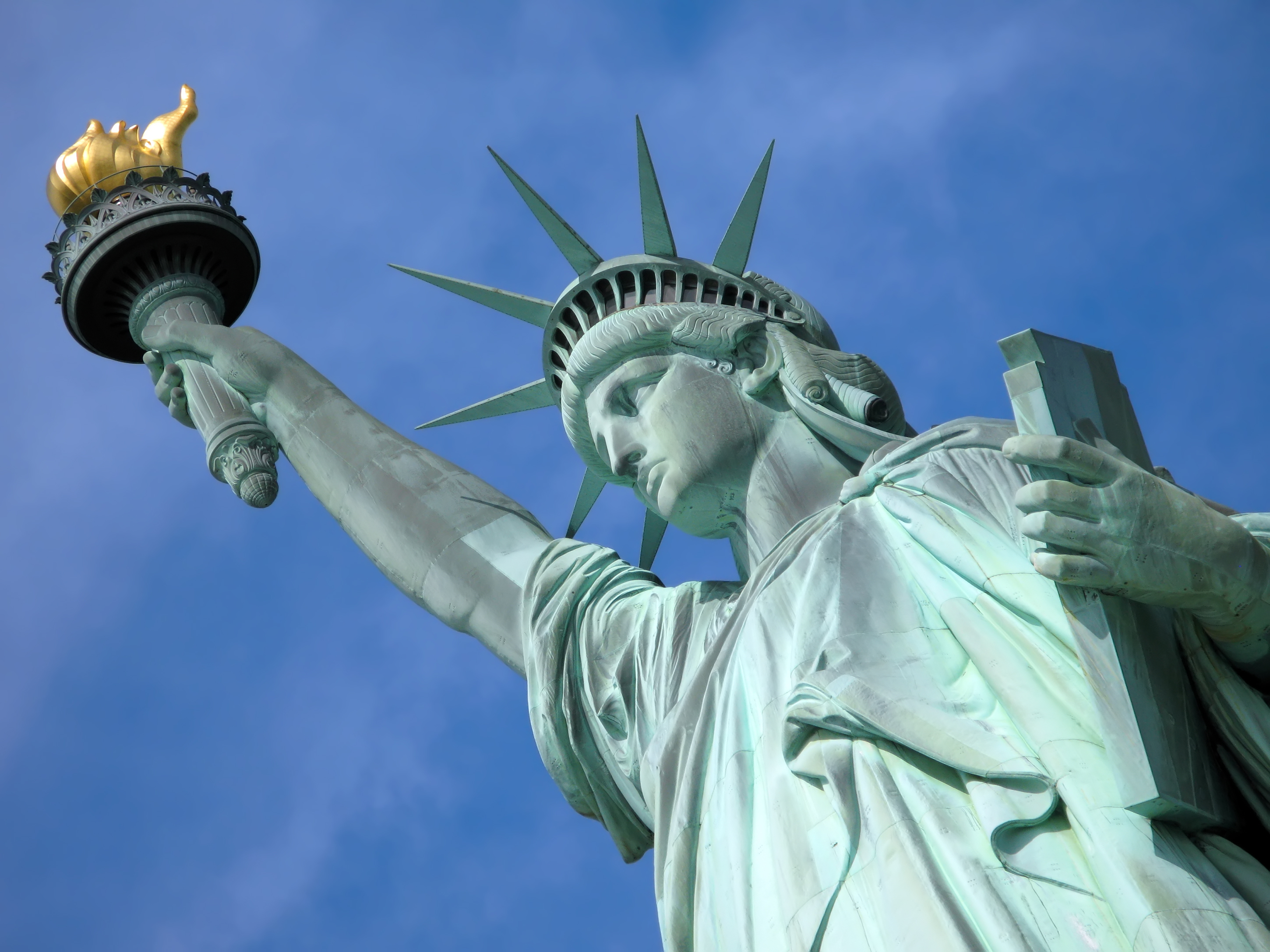 Nærbillede af Frihedsgudinden på Liberty Island i New York City med gyldent fakkel mod blå himmel