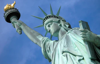 Nærbillede af Frihedsgudinden på Liberty Island i New York City med gyldent fakkel mod blå himmel