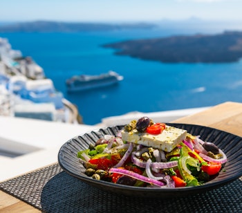 Traditionel græsk salat med friske grøntsager serveret med panoramaudsigt over Santorinis kaldera og det blå Ægæerhav