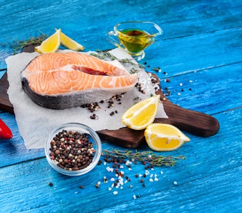 Frisk laksesteak på træskærebræt med citronskiver, chili og krydderier på blå træbaggrund, typisk nordisk madlavning