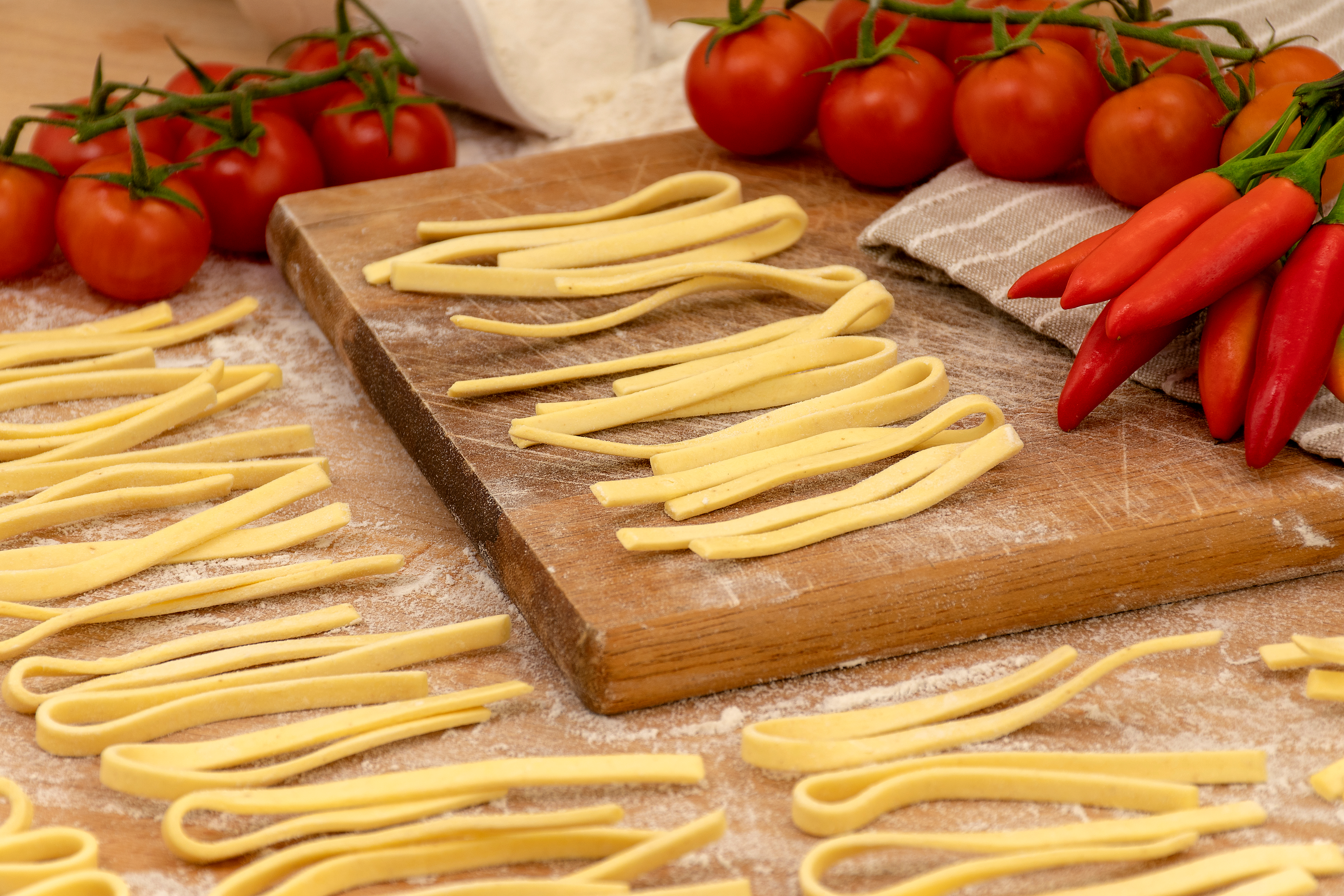 Frisklavet Scialatielli pasta fra Campania, Italien, med cherrytomater og røde chilipeber på et rustikt træskærebræt drysset med mel