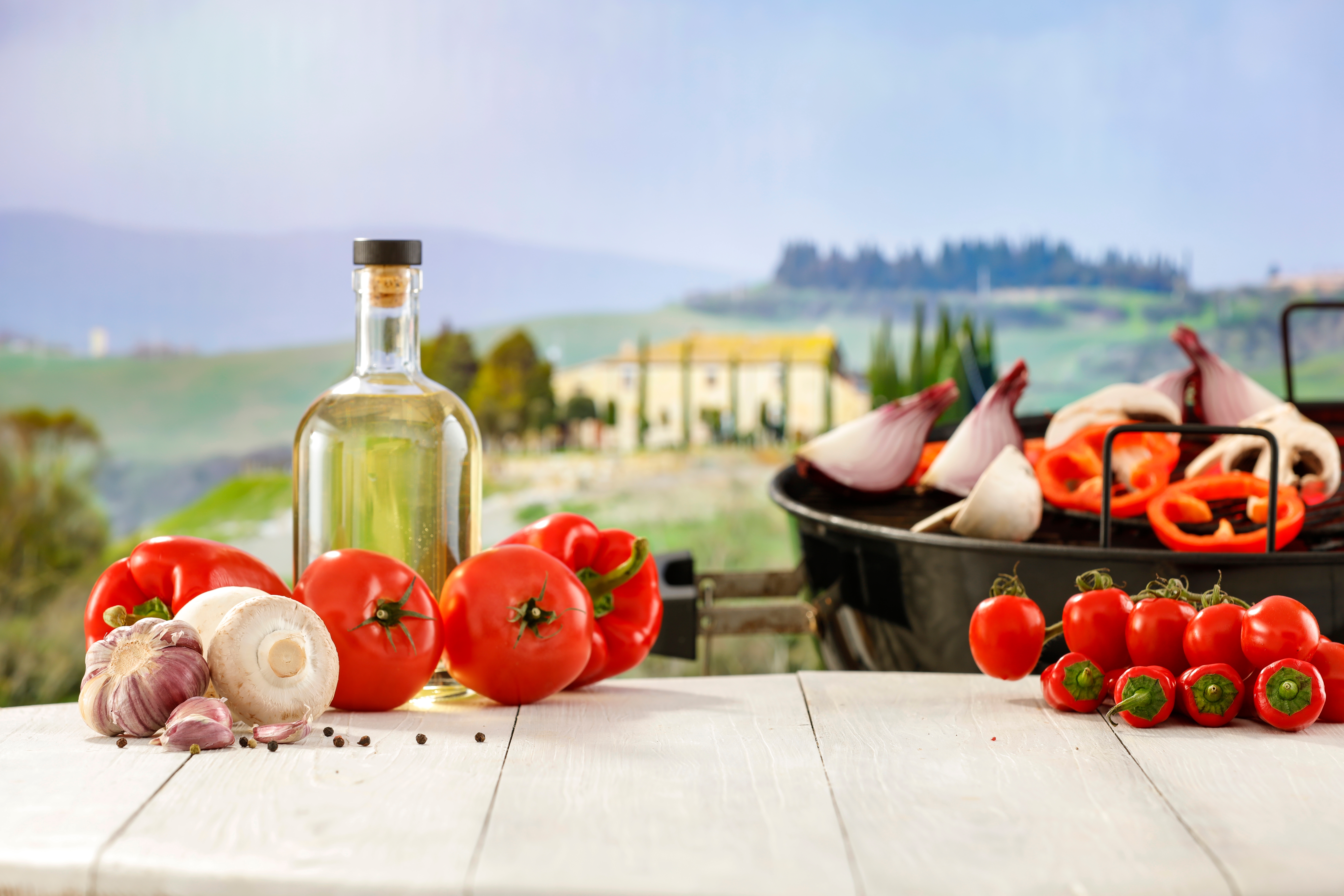Friske råvarer fra det toscanske køkken med olivenolie, tomater, hvidløg og grøntsager på rustikt træbord med udsigt over de smukke bakker i Toscana