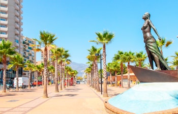 Idyllisk palmeklædt strandpromenade i Fuengirola ved Costa del Sol med blå himmel og udsigt over Middelhavet