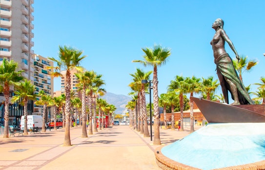 Idyllisk palmeklædt strandpromenade i Fuengirola ved Costa del Sol med blå himmel og udsigt over Middelhavet