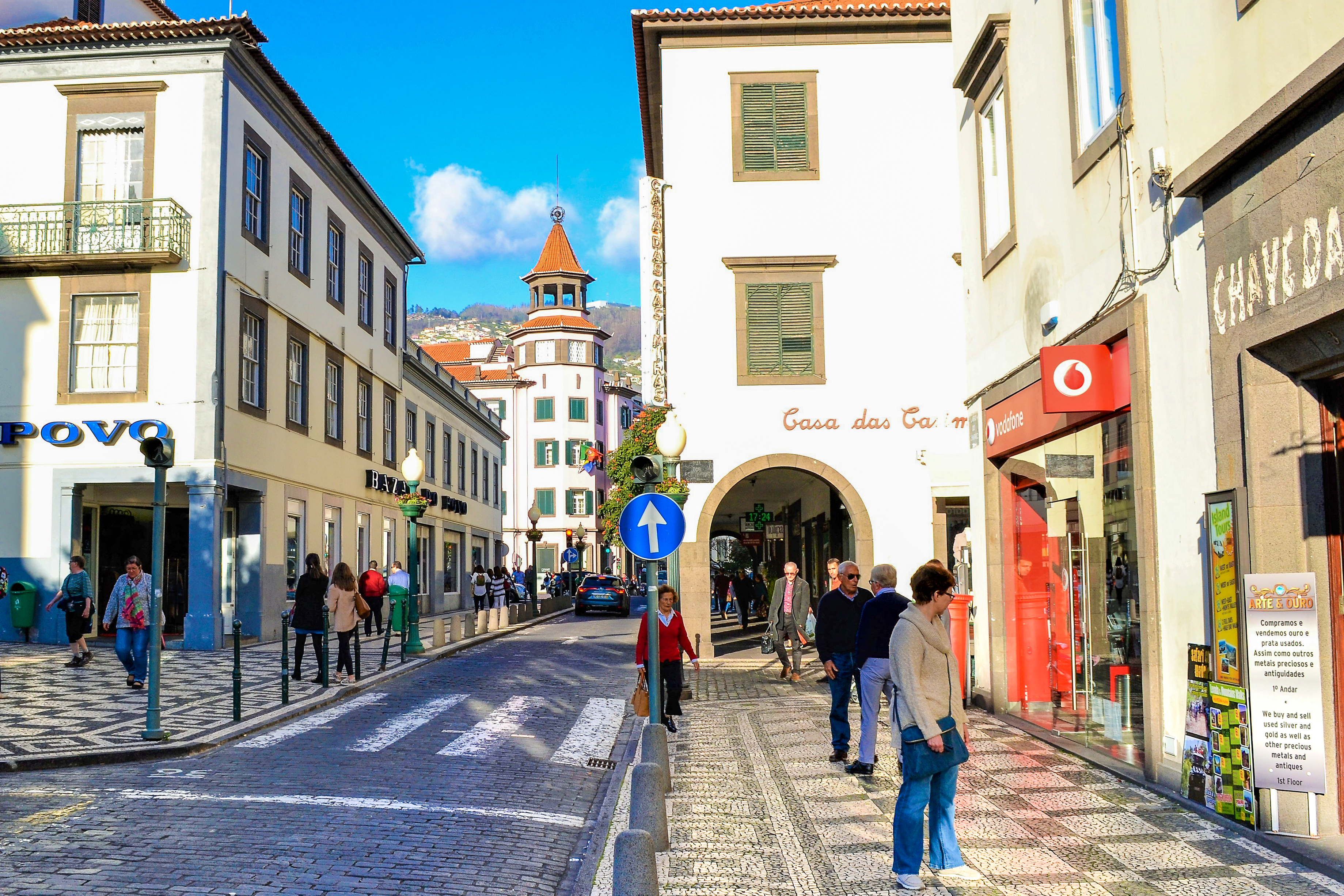 Solrig gade i centrum af Funchal på Madeira med brostensbelagte veje, charmerende portugisisk arkitektur, lokale butikker og turister der udforsker den historiske hovedby under blå himmel