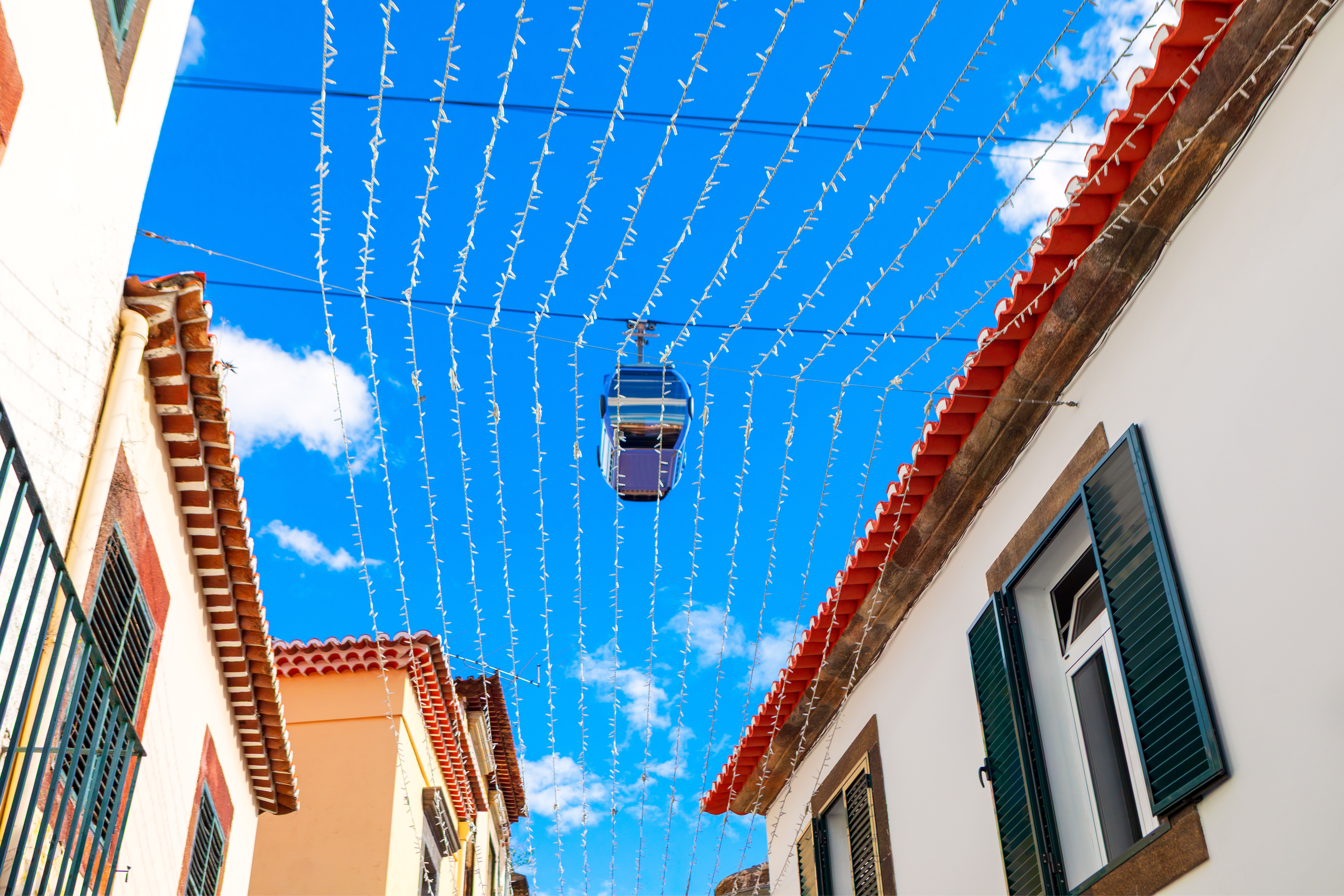 Kabelbane over Santa Maria-gaden i Funchal på Madeira, pyntet med julelys og guirlander spændt ud mellem farverige bygninger under blå himmel