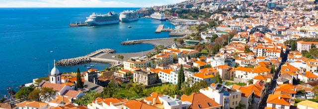 Luftudsigt over Funchal på Madeira med farverige bygninger, orange tegltage, havn med krydstogtskibe og den smukke atlanterhavskyst omgivet af bjerge