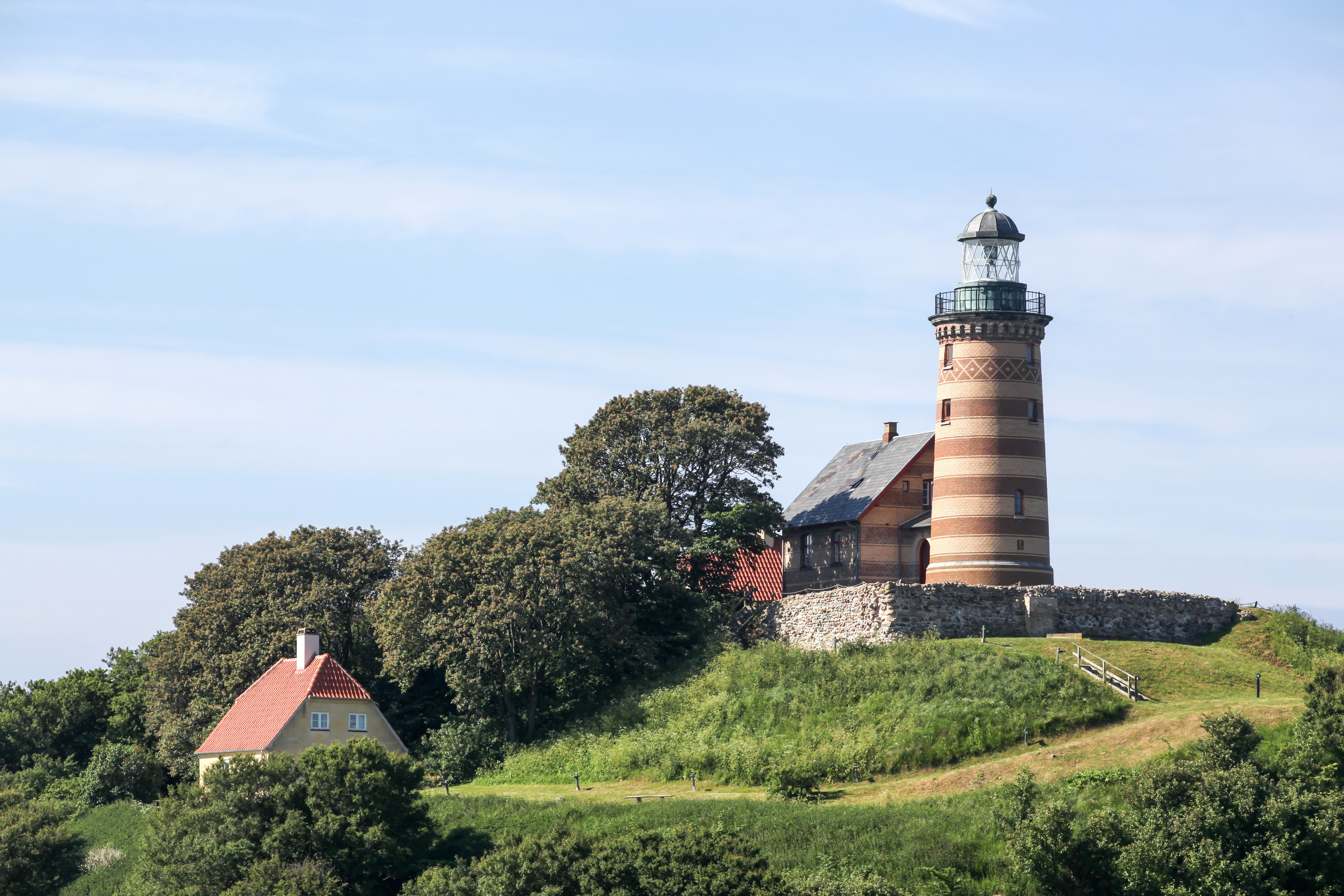 Historisk fyrtårn med røde og hvide striber på grøn bakke omgivet af traditionelle huse og frodige træer