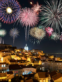 Farverigt fyrværkeri over Alfama-kvarteret i Lissabon med historiske bygninger og udsigt til Tagus-floden i nattelys