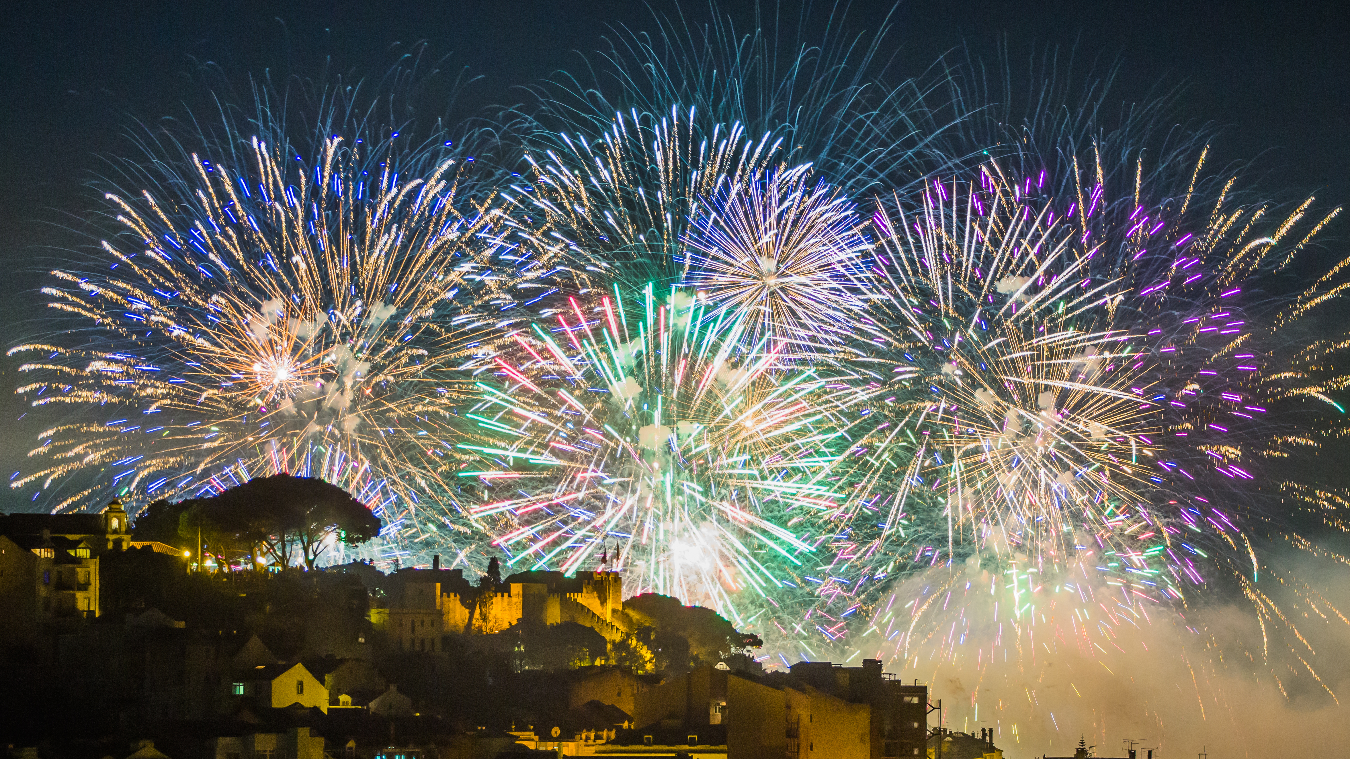 Spektakulært farverigt fyrværkeri over middelhavsby med historiske bygninger og kystlinje om natten