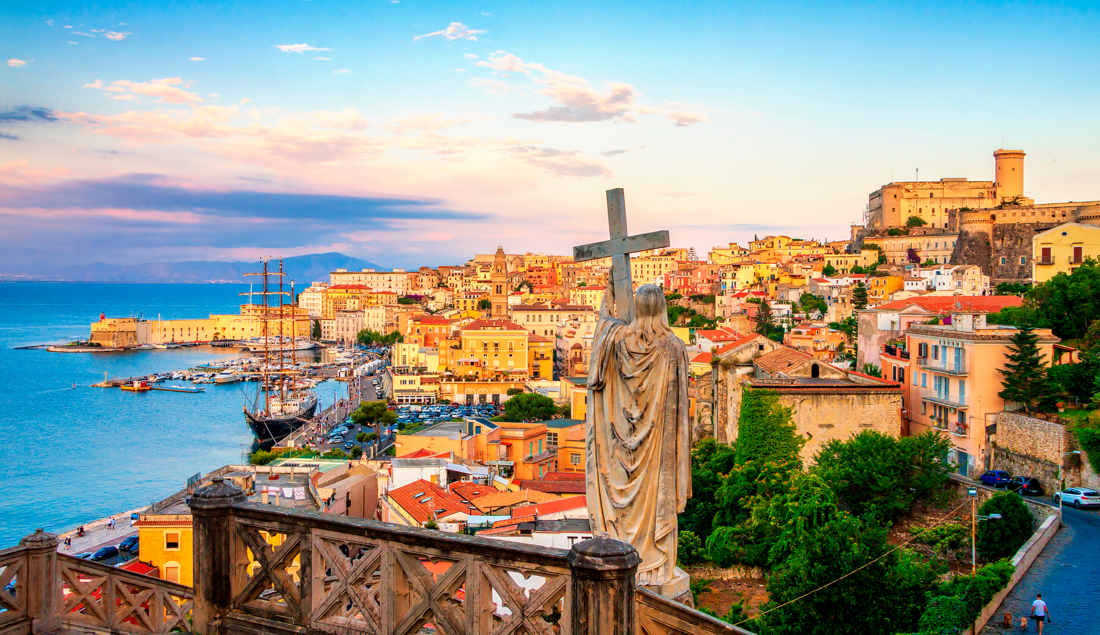 Panoramaudsigt over Gaeta i Italien med farverige bygninger, historisk havn og statue af Sankt Francesco ved solnedgang