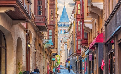 Charmerende smal gade med historiske stenbygninger der fører til det ikoniske Galata-tårn i Istanbuls Beyoglu-distrikt