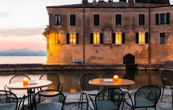 Stemningsfuld solnedgang over Gardasøen ved Punta San Vigilio med udsigt over det rolige vand og den naturskønne kyst i Norditalien