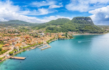 Betagende luftfoto af Garda by ved Gardasøens turkisblå vand med farverige bygninger og grønne bjerge i baggrunden, perfekt til en italiensk ferie