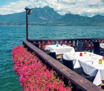 Romantisk restaurant med blomstersmykket terrasse direkte ved Gardasøens turkisblå vand med udsigt til bjergene