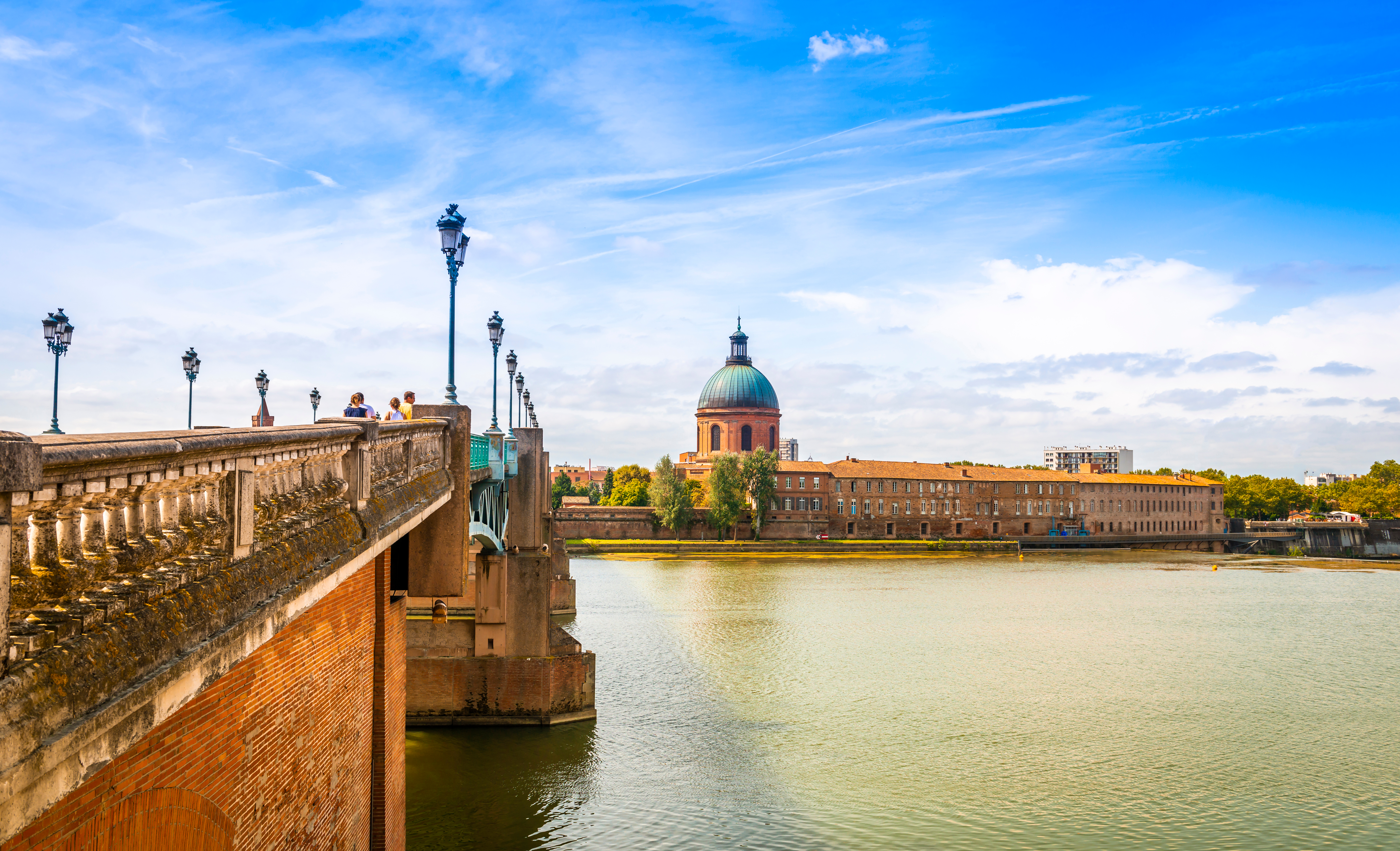 Garonne-floden med historiske broer og Toulouses smukke skyline ved solnedgang, hvor den lyserøde bys bygninger spejler sig i vandet under den blå aftenhimmel