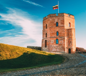 Gediminas-tårnet i Vilnius, Litauens historiske vartegn med det litauiske flag vajende fra toppen mod en blå himmel