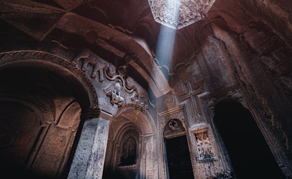 Fascinerende interiør i det klippeudhugne Geghard-kloster i Armenien, hvor en dramatisk lysstråle oplyser et ældgammelt basrelief med løvefigurer