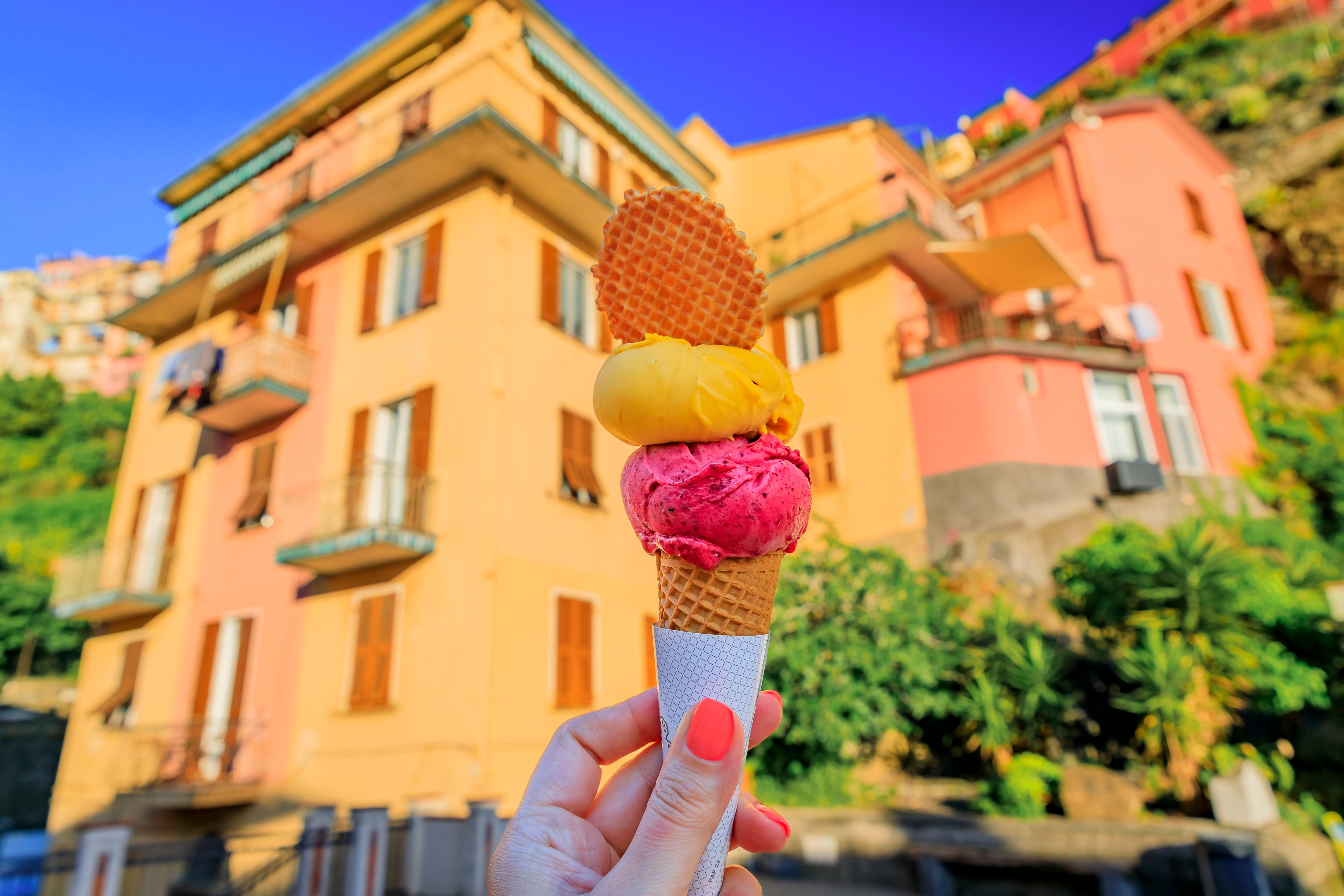 Hånd der holder italiensk gelato med cookie og udsigt til farverige huse i Manarola, Cinque Terre