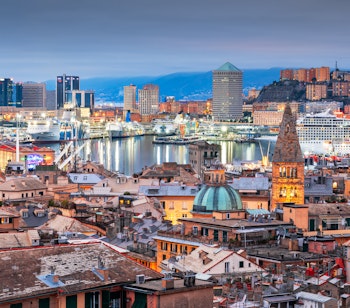 Genovas maleriske havnefront og byens skyline ved skumringstid, hvor historiske tårne møder moderne arkitektur i den italienske middelhavsby