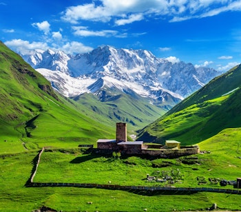 Historisk stentårn i grøn dal med snedækkede Kaukasus bjerge i Georgien