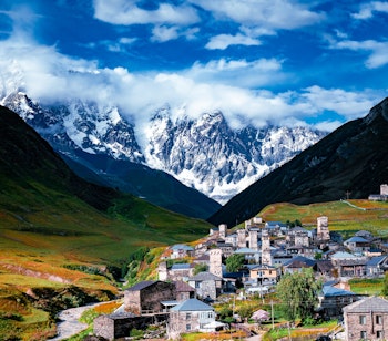 Traditionel georgisk bjerglandsby med middelalderlige stentårne i Svaneti-regionen omgivet af snedækkede Kaukasus-bjerge