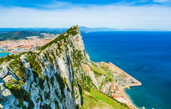 Betagende luftfoto af Gibraltarklippen med den blå Middelhavskyst og byen Gibraltar ved foden, et imponerende britisk landemærke på den Iberiske Halvø