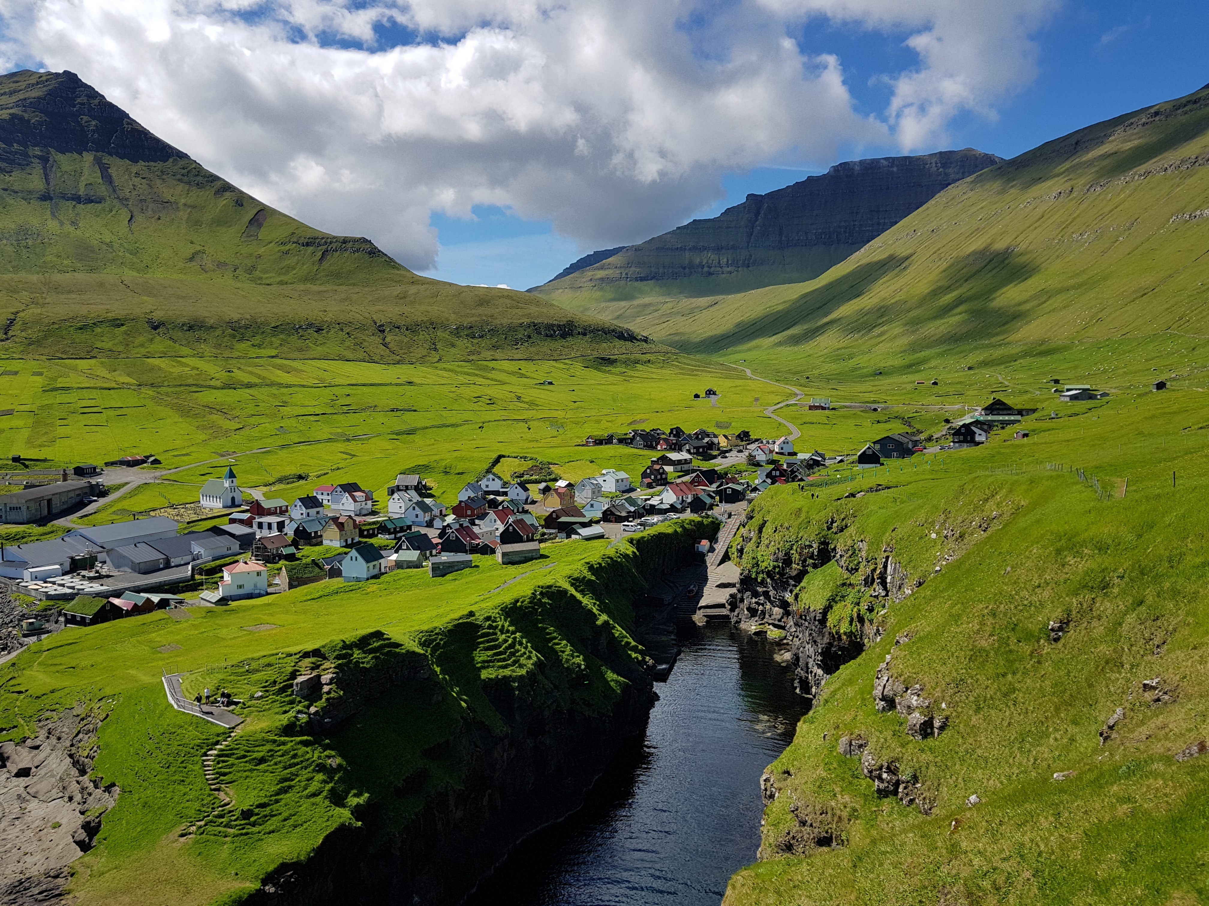 Idyllisk sommerlandskab over Gjógv landsby på Færøerne med grønne bjerge og blå himmel