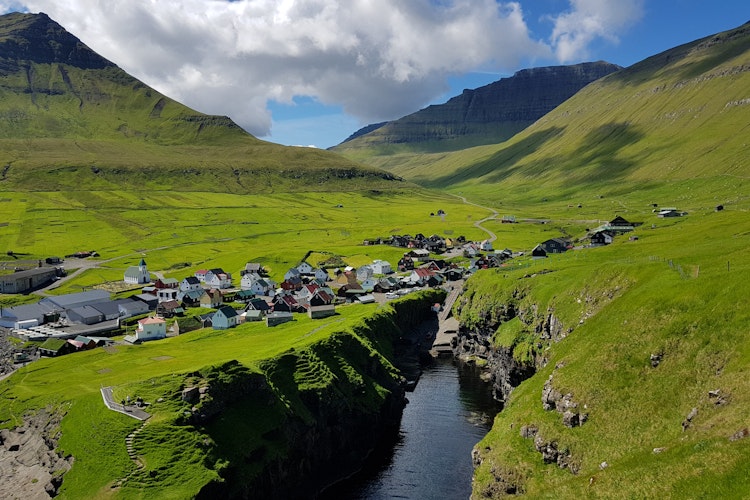 Idyllisk sommerlandskab over Gjógv landsby på Færøerne med grønne bjerge og blå himmel