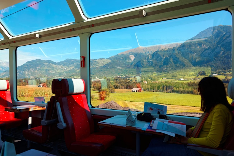 Passager nyder den betagende udsigt over de schweiziske alper gennem panoramavinduer på Glacier Express luksustoget på en solrig sommerdag