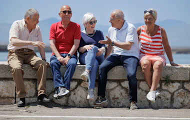 Gruppe af glade seniorer nyder sommerferie sammen ved marina