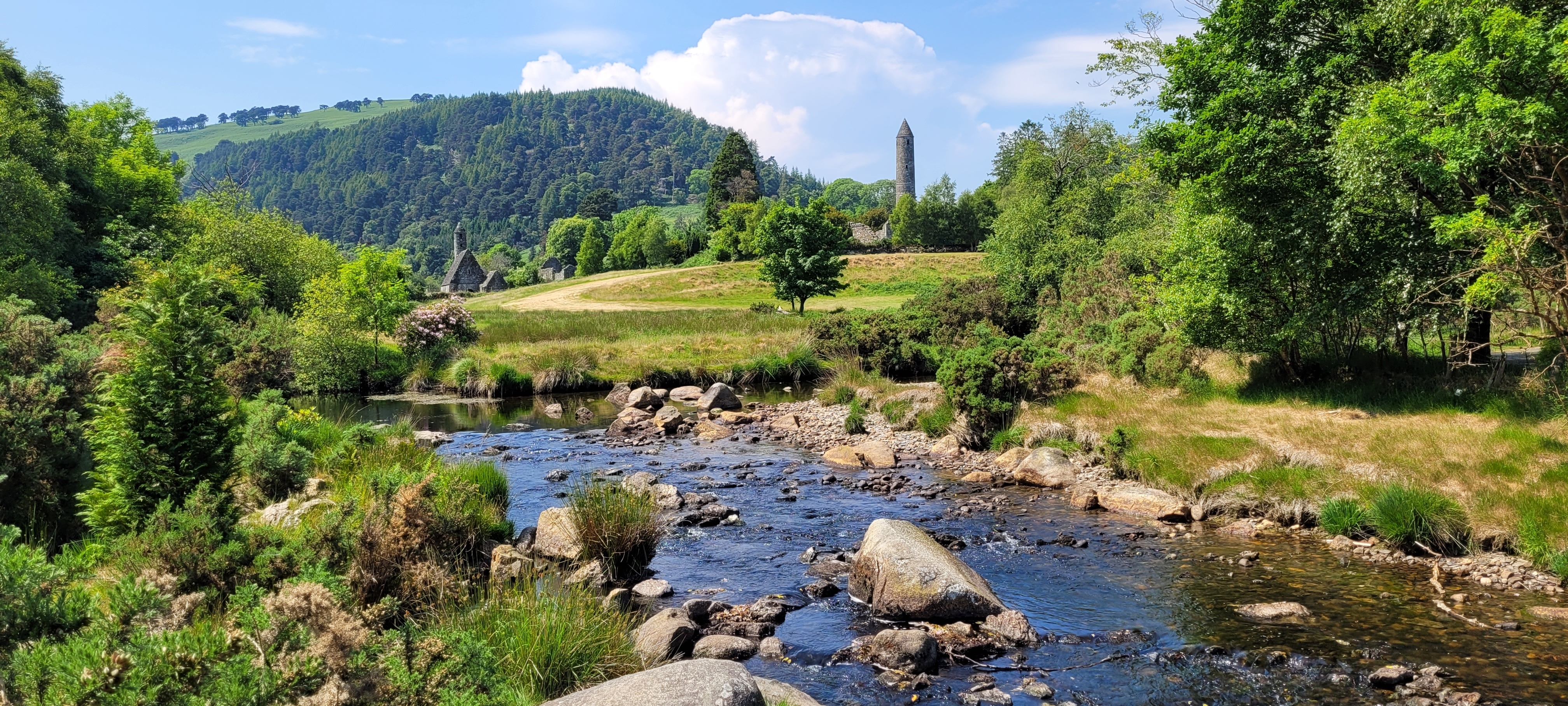 Stenet å løber gennem det historiske klosteranlæg Glendalough med det karakteristiske rundtårn omgivet af frodig irsk natur i County Wicklow