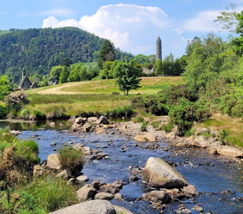 Stenet å løber gennem det historiske klosteranlæg Glendalough med det karakteristiske rundtårn omgivet af frodig irsk natur i County Wicklow