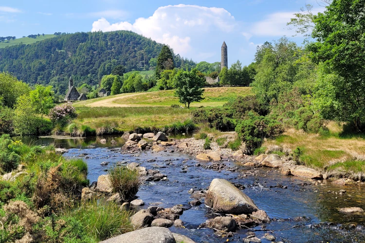 Stenet å løber gennem det historiske klosteranlæg Glendalough med det karakteristiske rundtårn omgivet af frodig irsk natur i County Wicklow