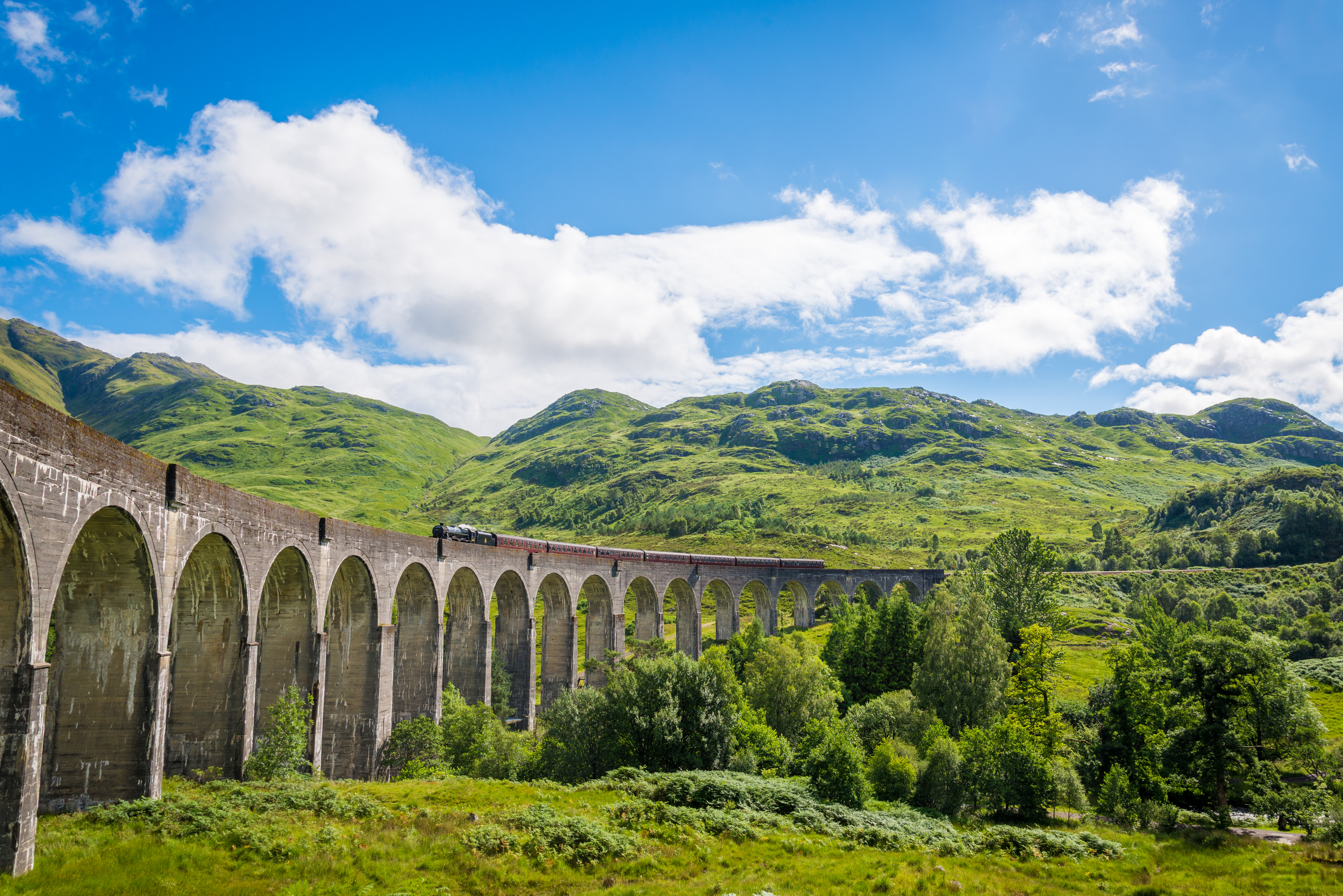 Historisk Glenfinnan Viadukt med damptog der krydser gennem Skotlands grønne højland