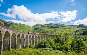 Historisk Glenfinnan Viadukt med damptog der krydser gennem Skotlands grønne højland