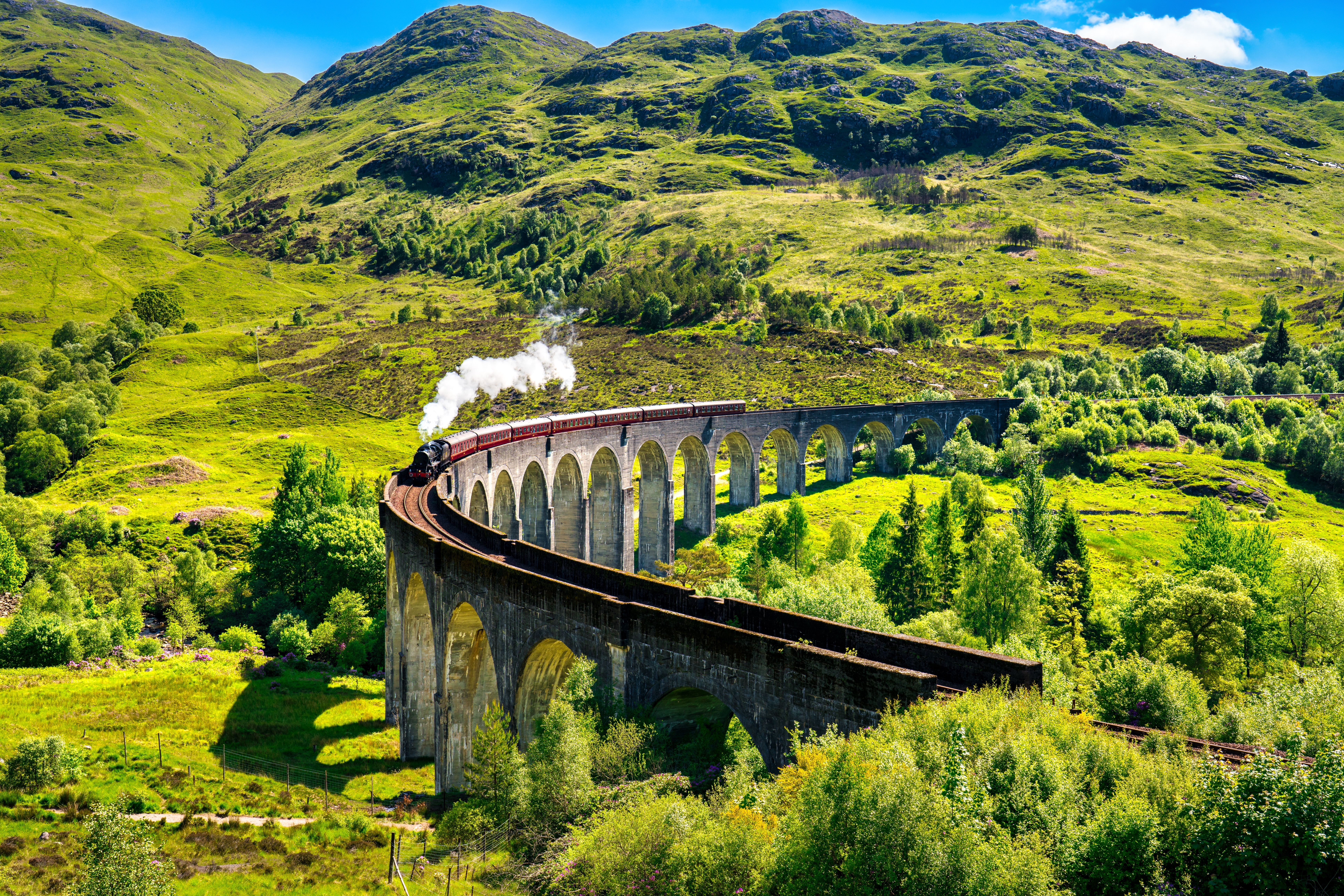 Den historiske Glenfinnan viadukt med damptog der krydser gennem det smukke skotske højland under en skyet himmel