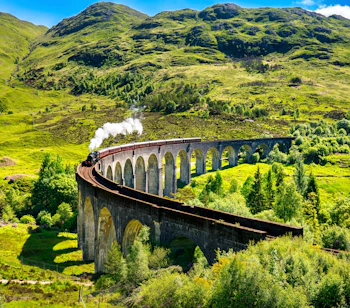 Den historiske Glenfinnan viadukt med damptog der krydser gennem det smukke skotske højland under en skyet himmel