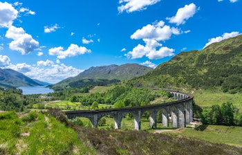 Den historiske Glenfinnan-viadukt i det skotske højland med sine karakteristiske buer omgivet af grønne bjerge under blå himmel