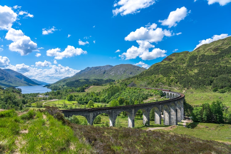 Den historiske Glenfinnan-viadukt i det skotske højland med sine karakteristiske buer omgivet af grønne bjerge under blå himmel