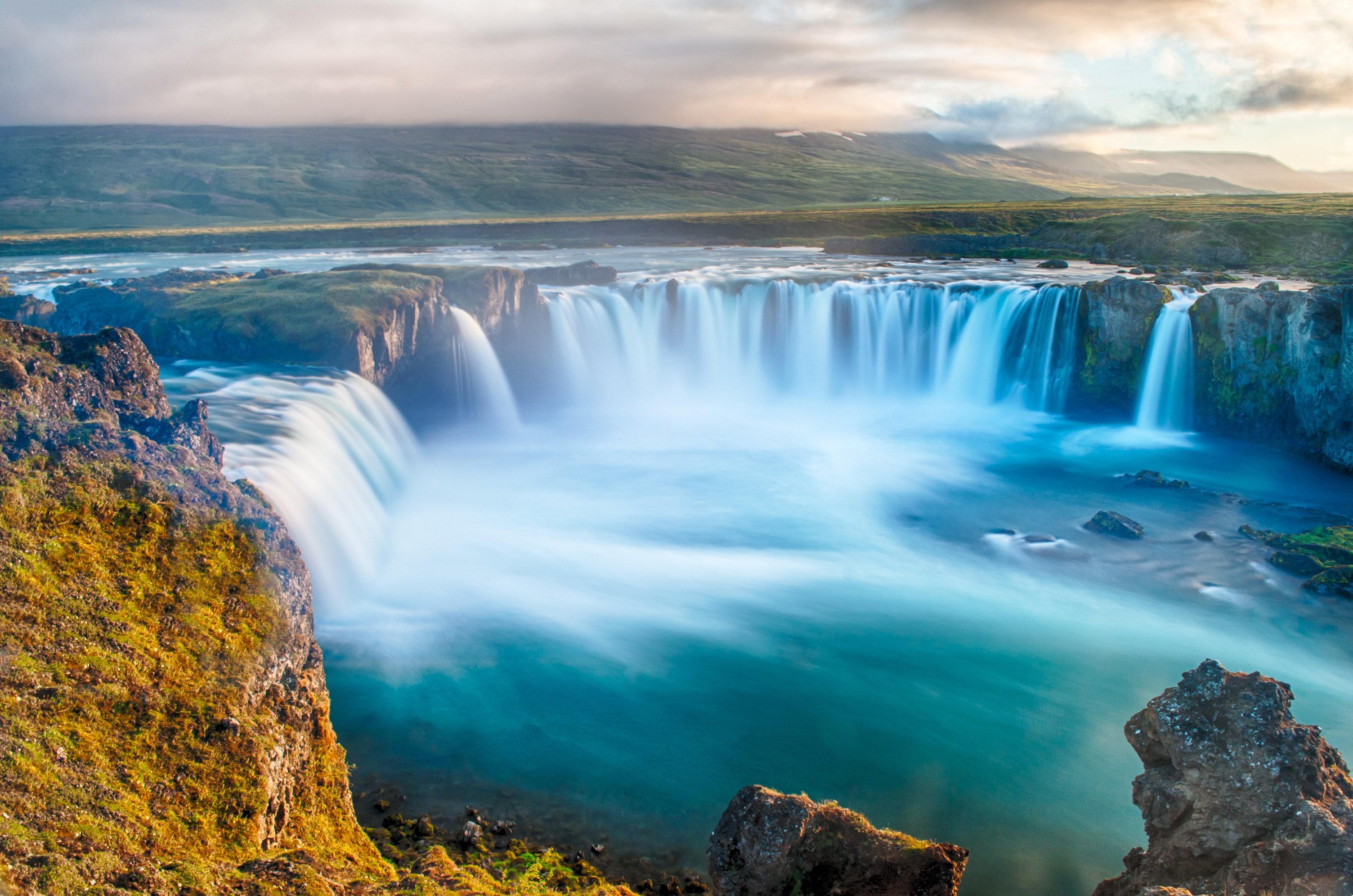 Det majestætiske Godafoss vandfald i Nordisland fotograferet under midnatssolen med dramatiske blå farver og kraftfuldt flydende vand