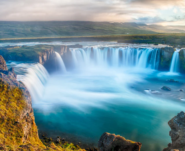 Det majestætiske Godafoss vandfald i Nordisland fotograferet under midnatssolen med dramatiske blå farver og kraftfuldt flydende vand