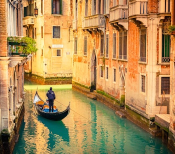 Traditionel gondol sejler gennem en smuk kanal i Venedig med farverige historiske bygninger der spejler sig i det turkise vand