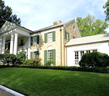 Graceland i Memphis, Tennessee – Elvis Presleys berømte hjem med hvide søjler og grønne skodder omgivet af grøn græsplæne